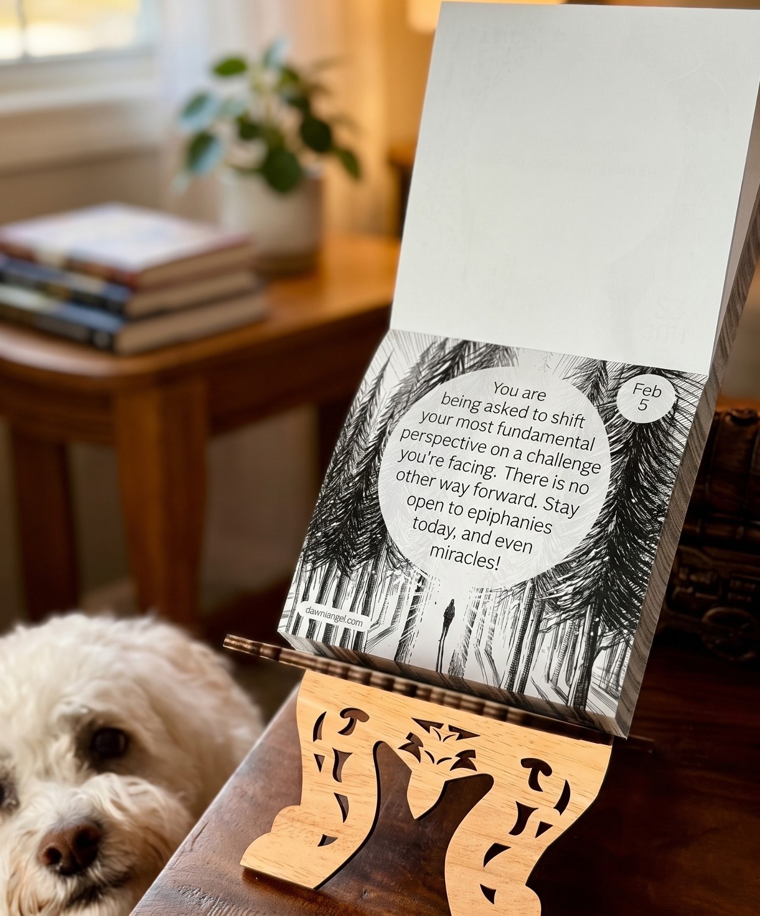 The calendar open to February 5 on a carved wooden stand, the day's message inside a circle of light between line-drawn pine trees, with a small white dog looking on.